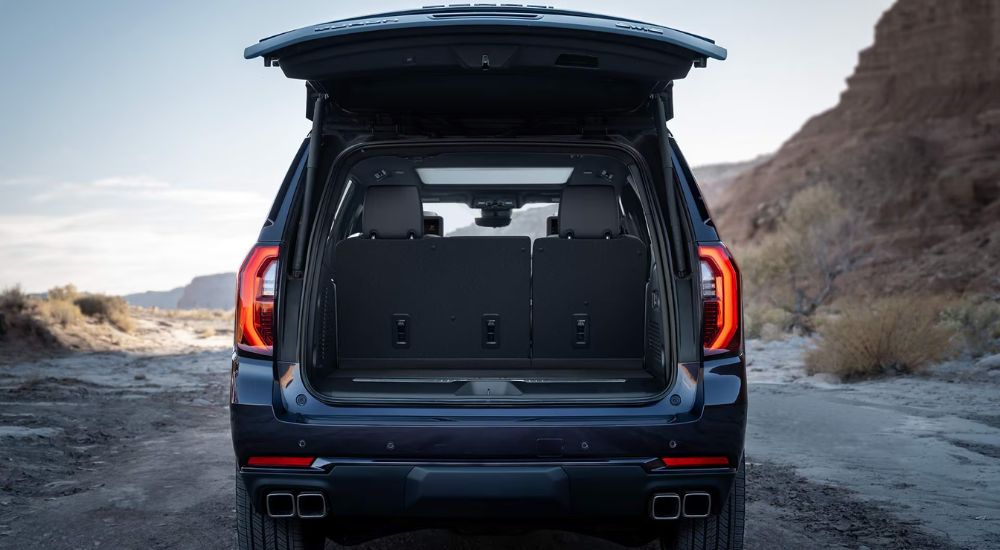 Blue 2027 GMC Yukon with an open lift gate parked off-road in the sand.