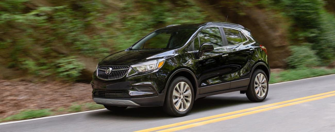 Black 2020 Buick Encore driving near a forest.