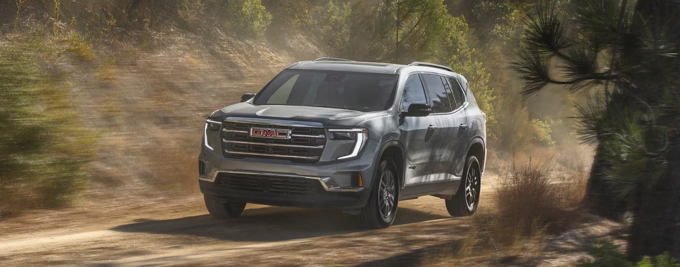 Grey 2025 GMC Acadia driving on an off-road trail.