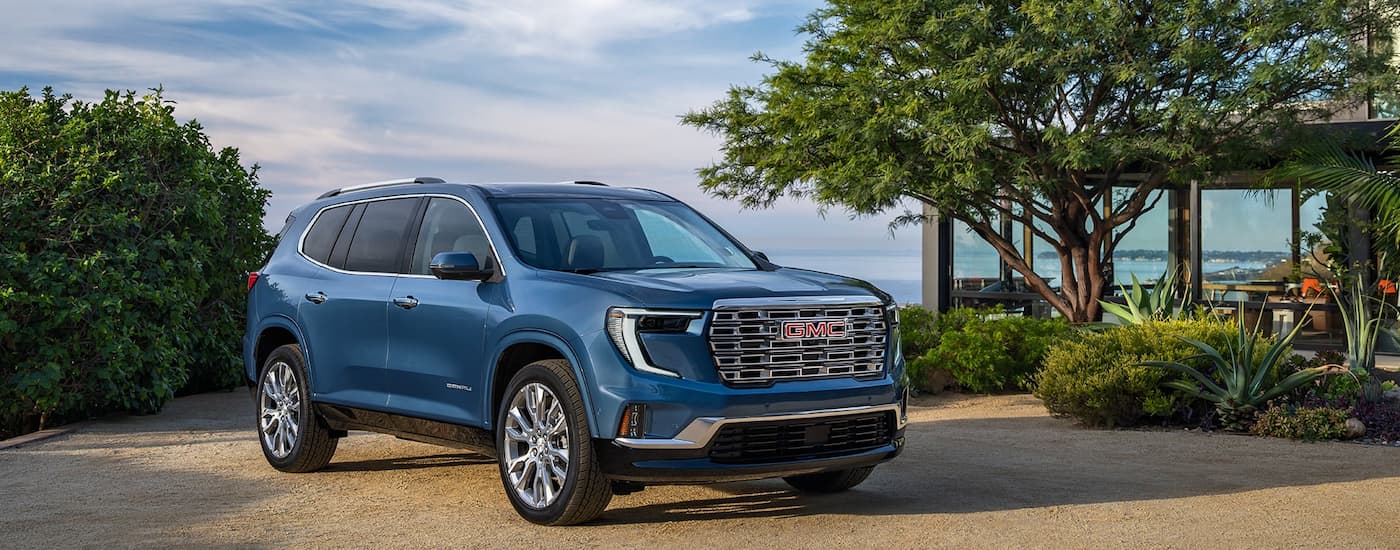 Blue 2026 GMC Acadia parked on a driveway outside of a house.