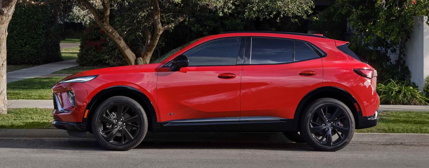 Red 2026 Buick Envision ST parked on a tree-lined street.