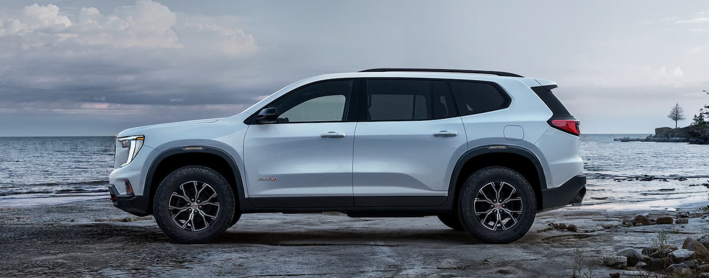 Side of a white 2026 GMC Acadia parked off-road near a lake.