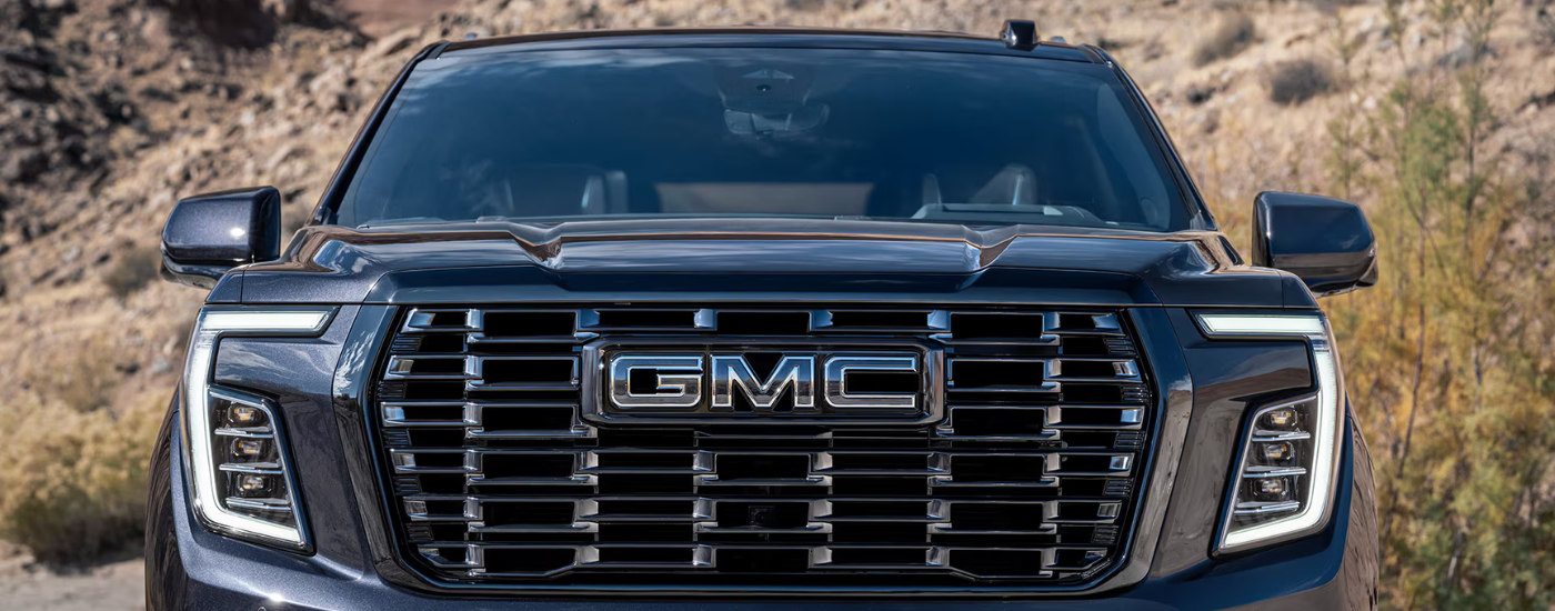 Front view of a black grille and badging on a grey 2026 GMC Yukon XL Denali