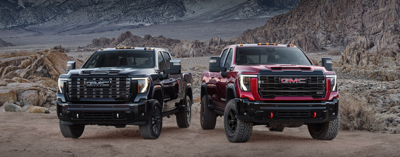 A black 2027 GMC Sierra 2500 Denali HD next to a red 2027 GMC Sierra 2500 AT4X HD in a canyon