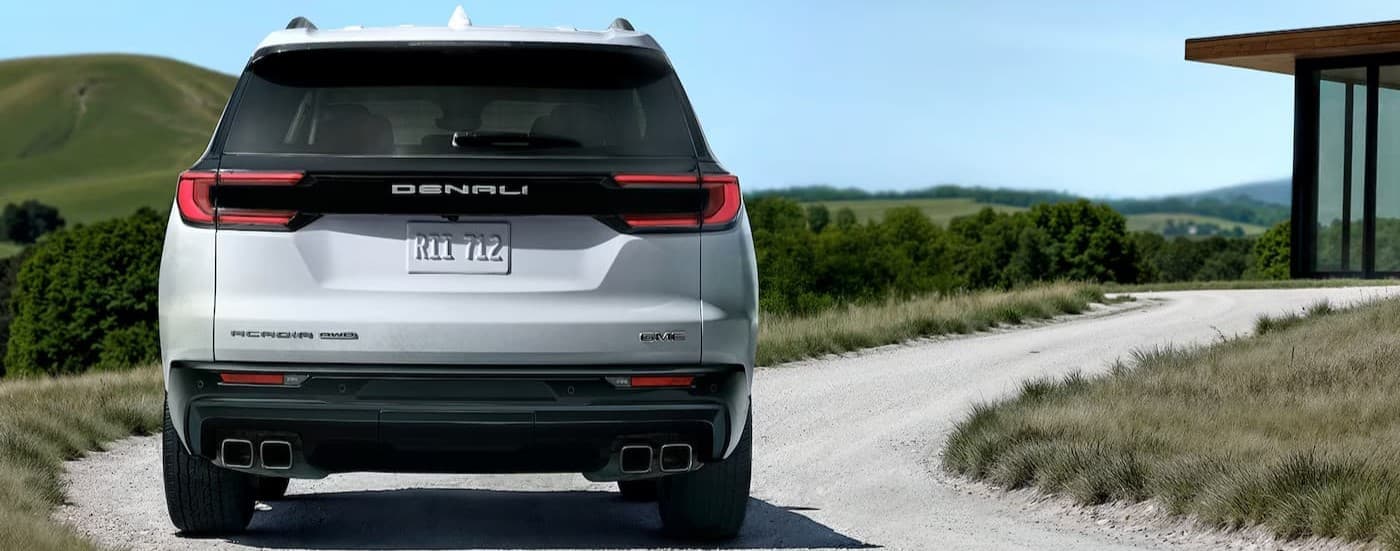 A white 2026 GMC Acadia driving on a backroad.